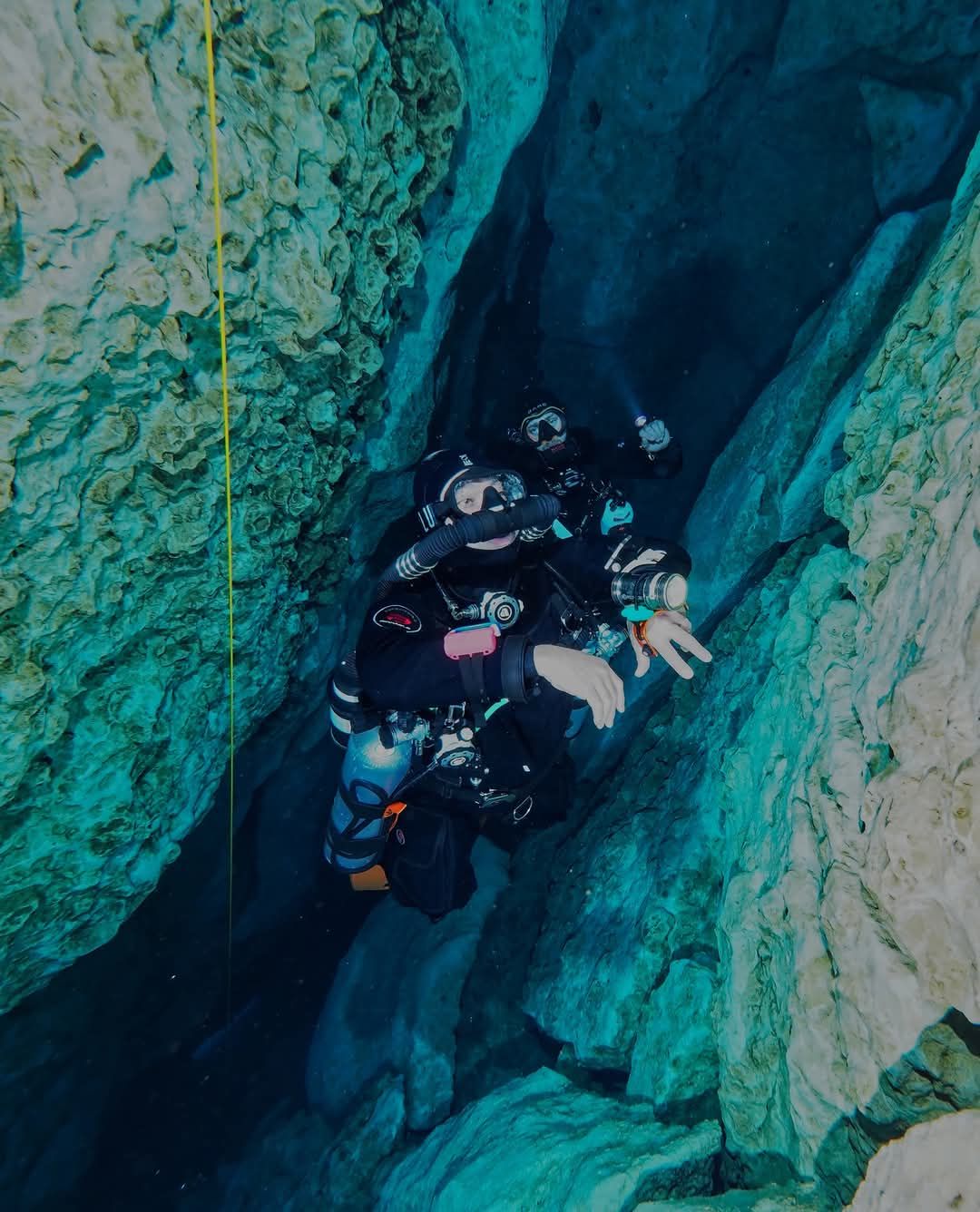 Two divers on closed-circuit rebreathers following the line through a narrow blue cave passage in North Florida