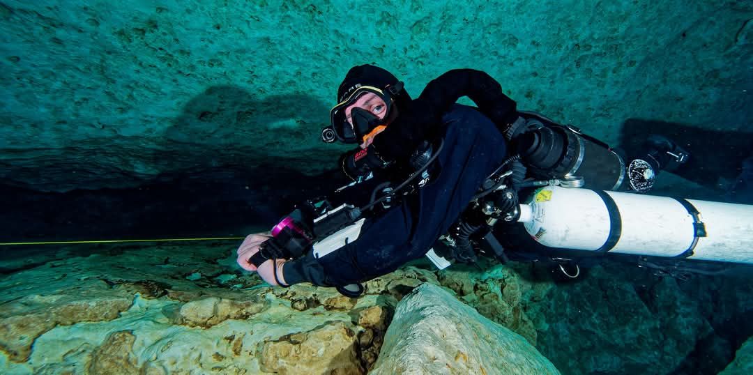 Sidemount cave diver with two cylinders following the guideline over limestone